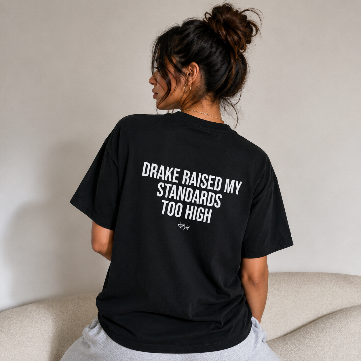 Person wearing a black t-shirt with text on the back, sitting on a couch.