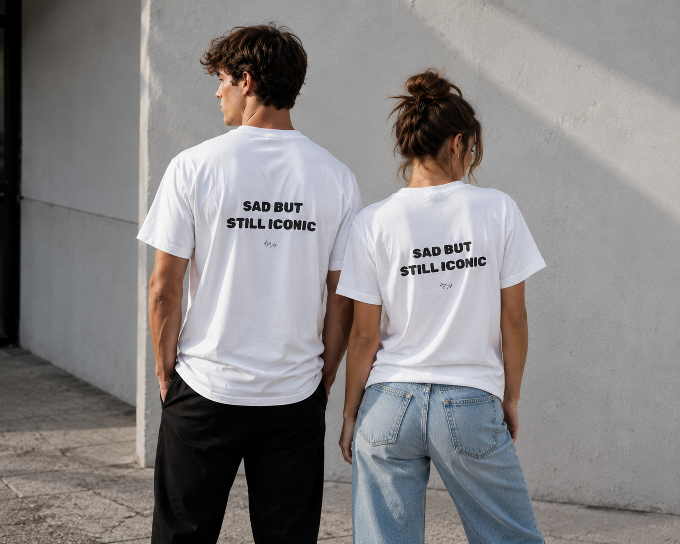 Two people wearing white t-shirts with text on the back, standing against a light-colored wall.